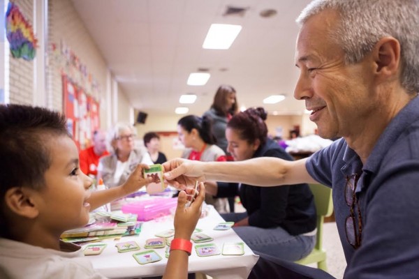 MCALLEN, TEXAS – SEPTEMBER 5: Joaquin Duato, Worldwide Chairman of Pharmaceuticals for Johnson and Johnson plays with a young Central American immigrant boy at the Sacred Heart Church in McAllen, TX where recently arrived families from Central America have received shelter and aid before traveling on to their final destinations within the United States, on Friday, September 5, 2014.  (Photo by Scott Dalton/Global Assignment by Getty Images for Save the Children)